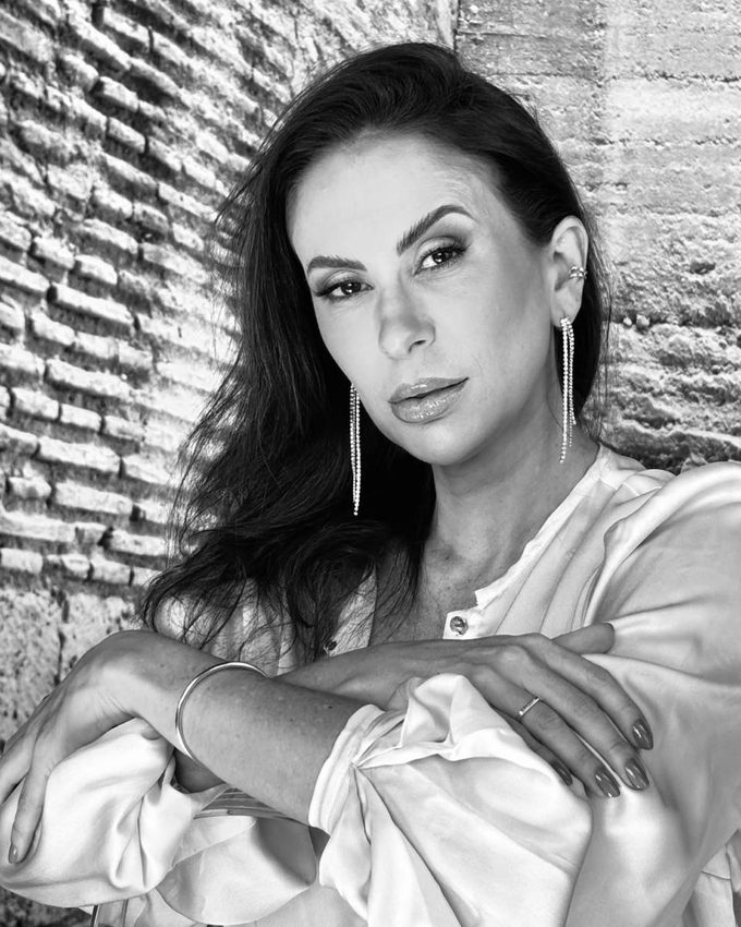 Retrato em preto e branco da Dra. Priscilla Carneiro diante de uma parede de tijolos antigos